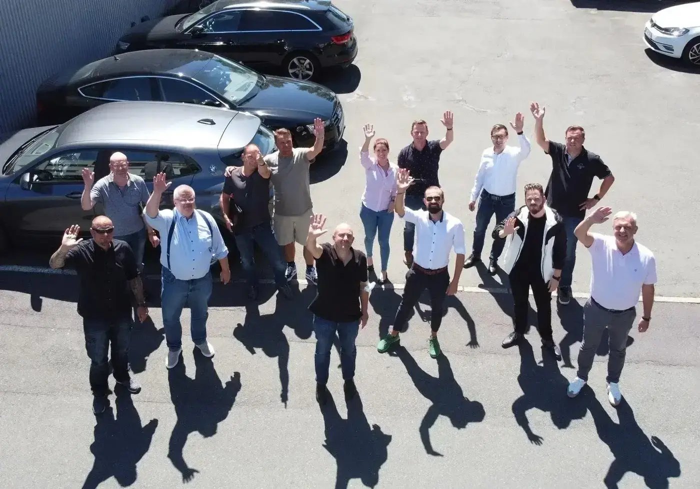 Das lichtline Vertriebs-Team winkt gemeinsam auf einem Parkplatz vor dem Firmengebäude.